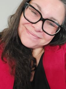A smiling woman with long, dark hair wearing large black glasses and a red blazer.